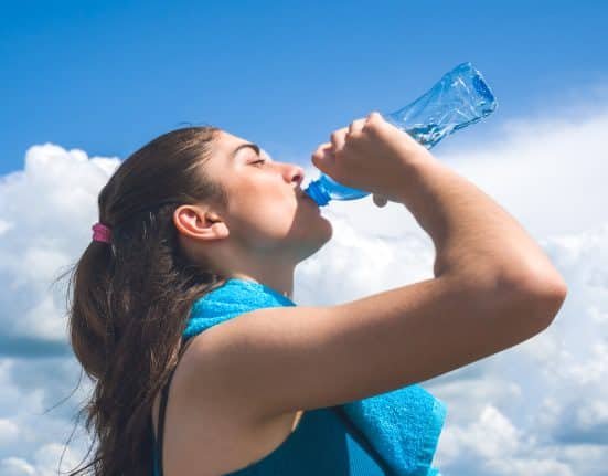 Beautifull girl runner is having break, drinking water against c