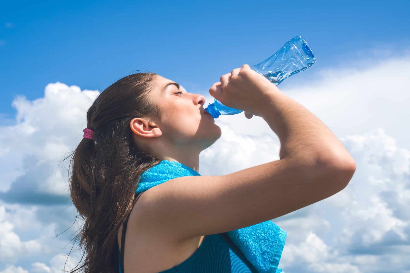 Beautifull girl runner is having break, drinking water against c