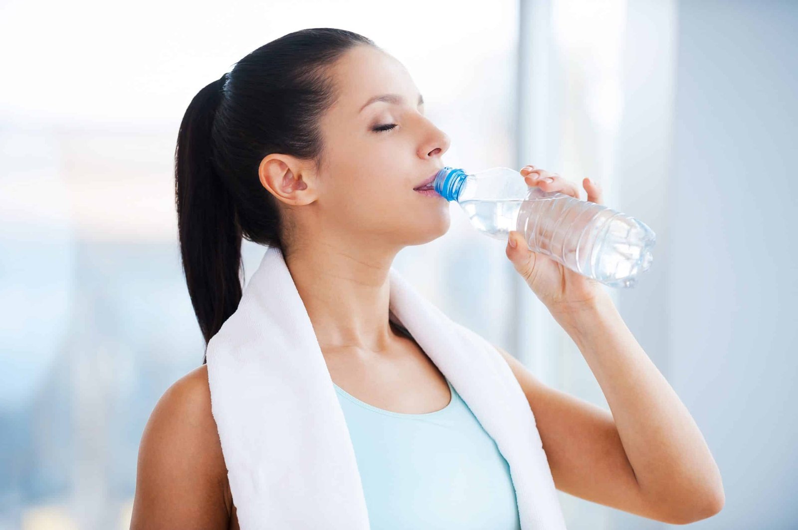 Refreshing after workout. Beautiful young woman in sports clothing drinking water and keeping eyes closed while standing in health club